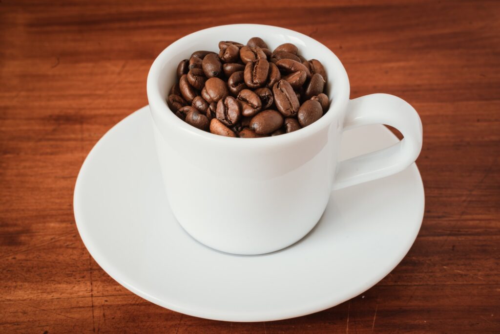 White cup of coffee and saucer filled with coffee beans
